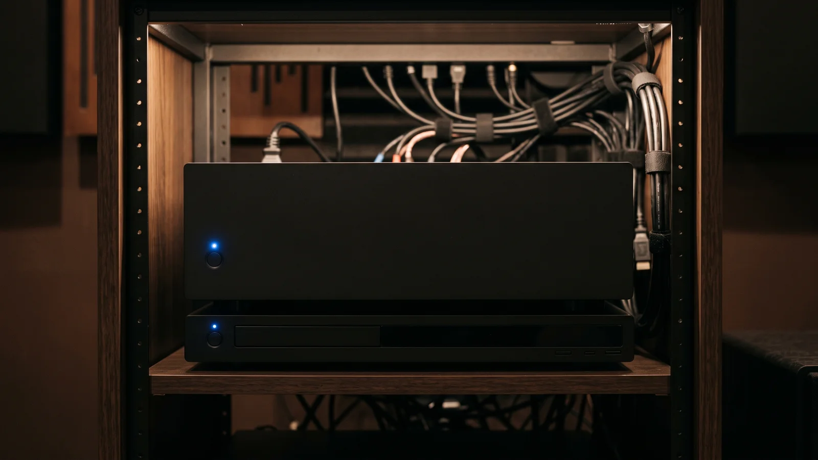 A black AV receiver and a disc player stacked in a home-theater equipment rack with neatly managed cables behind them