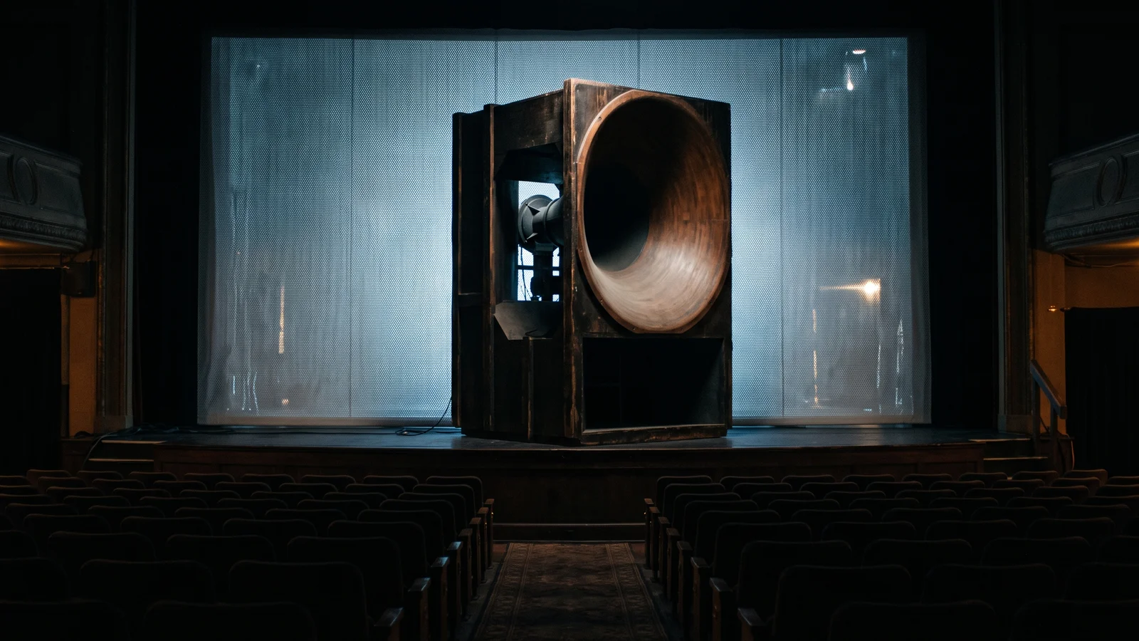 A vintage cinema folded horn loudspeaker standing behind a movie screen, evoking the Voice of the Theatre era
