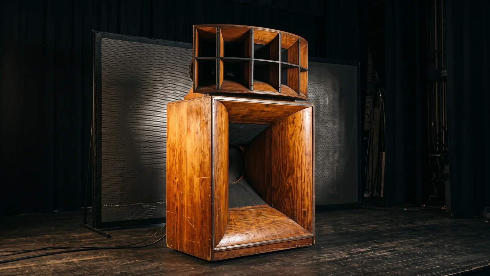 A vintage refrigerator-sized folded cinema horn loudspeaker standing behind a movie screen in a darkened auditorium