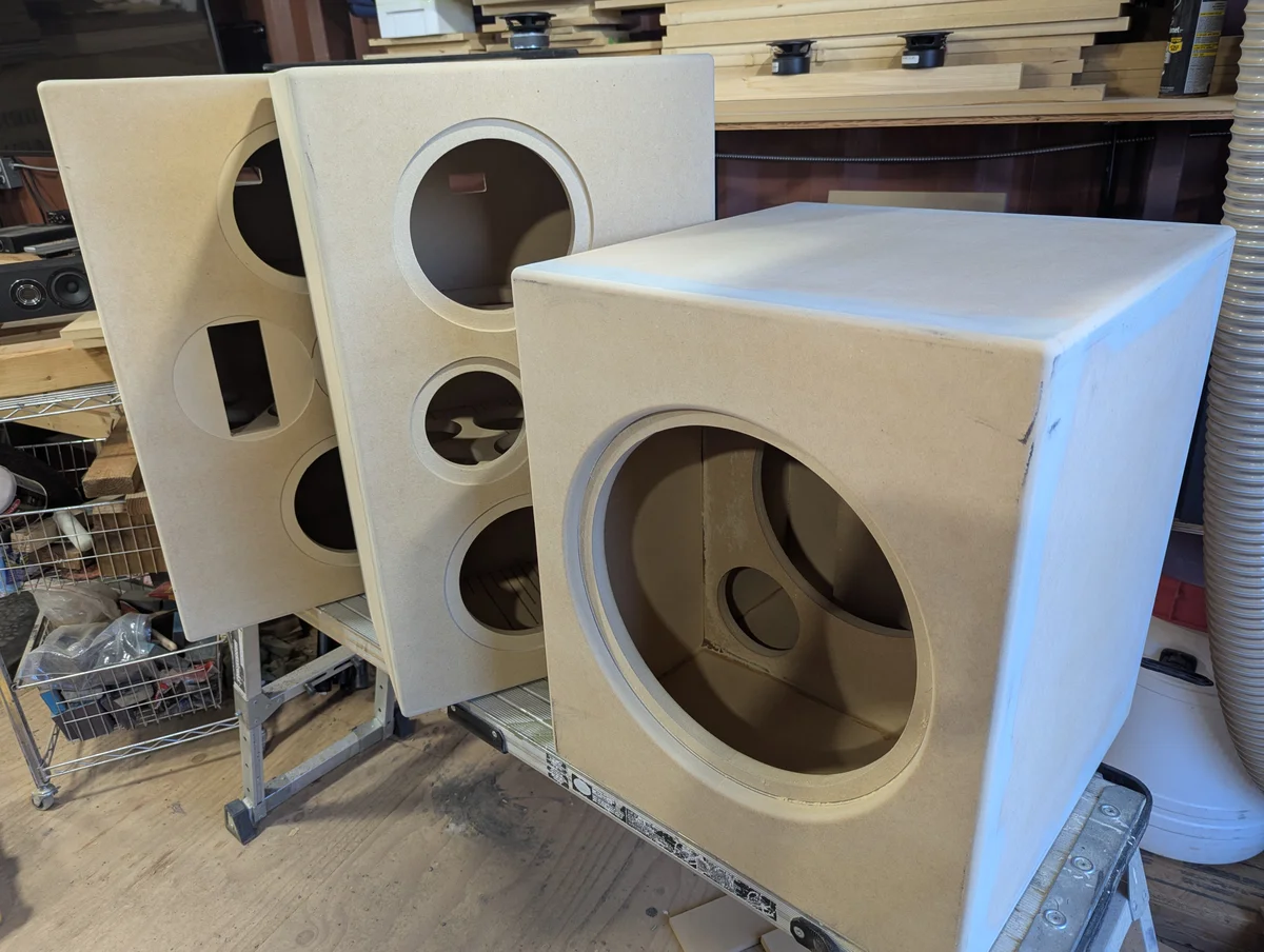 Unfinished bookshelf and subwoofer cabinets showing internal bracing and driver cutouts